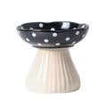 Ceramic bowl with black top and white polka dots on a beige stand against a white background